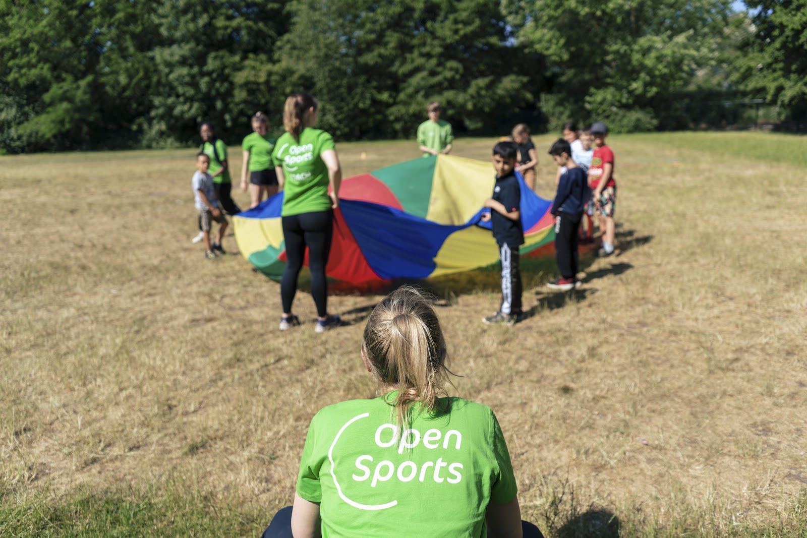 Coaches von Open Sports spielen mit Kindern unter einem Schwungtuch